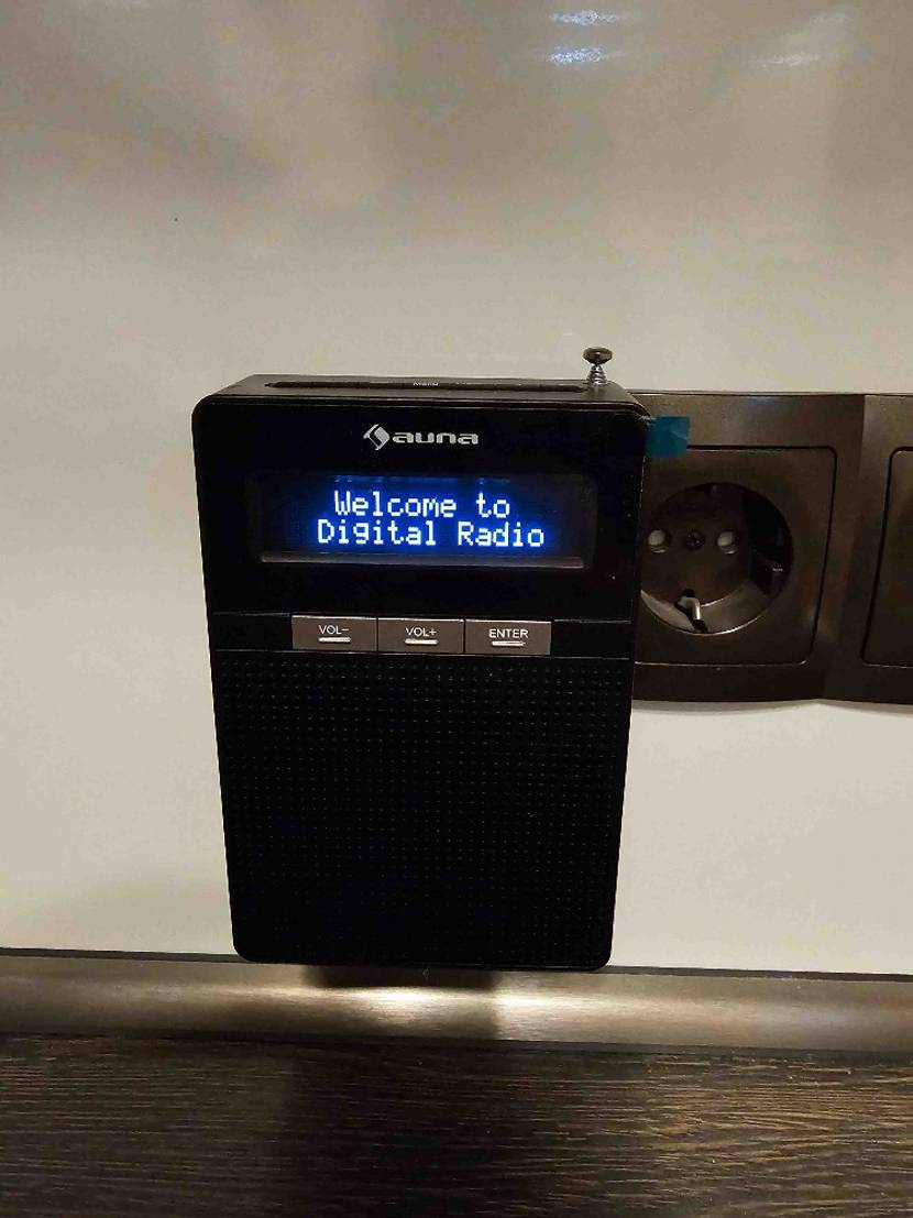 Ein eingeschaltenes Steckdosenradio im Test mit Anzeige auf dem Display von vorne in einer Steckdosenleiste an der Wand.