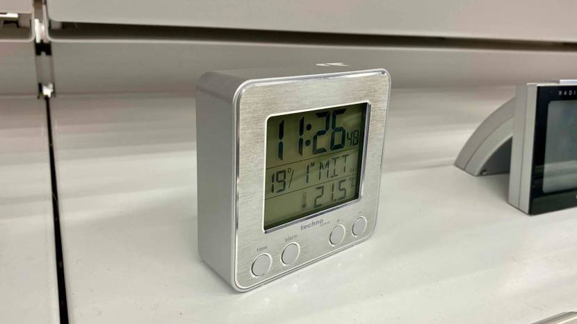Ein getesteter Funkwecker von schräg seitlich mit angeschaltetem Display in einem hellen Verkaufsregal.