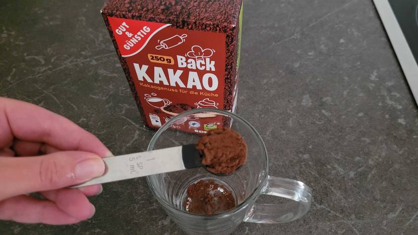 Kakaopulver wird dosiert und in Glastasse gekippt.