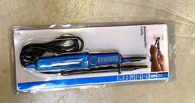 Ein blauer Spannungsprüfer im Test der Marke Unitec liegt in der Originalverpackung auf einem hellgrauen Betonboden.
