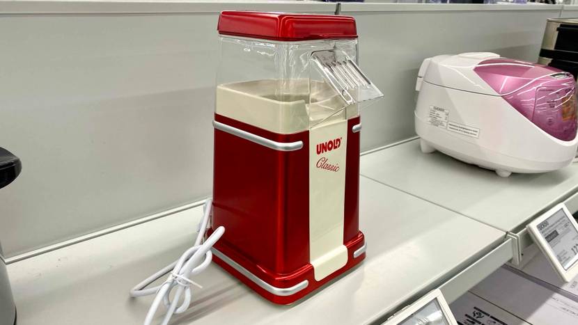 Eine getestete Popcornmaschine von leicht seitlich auf einem Verkaufsregal mit anderen Geräten und Preisangaben.
