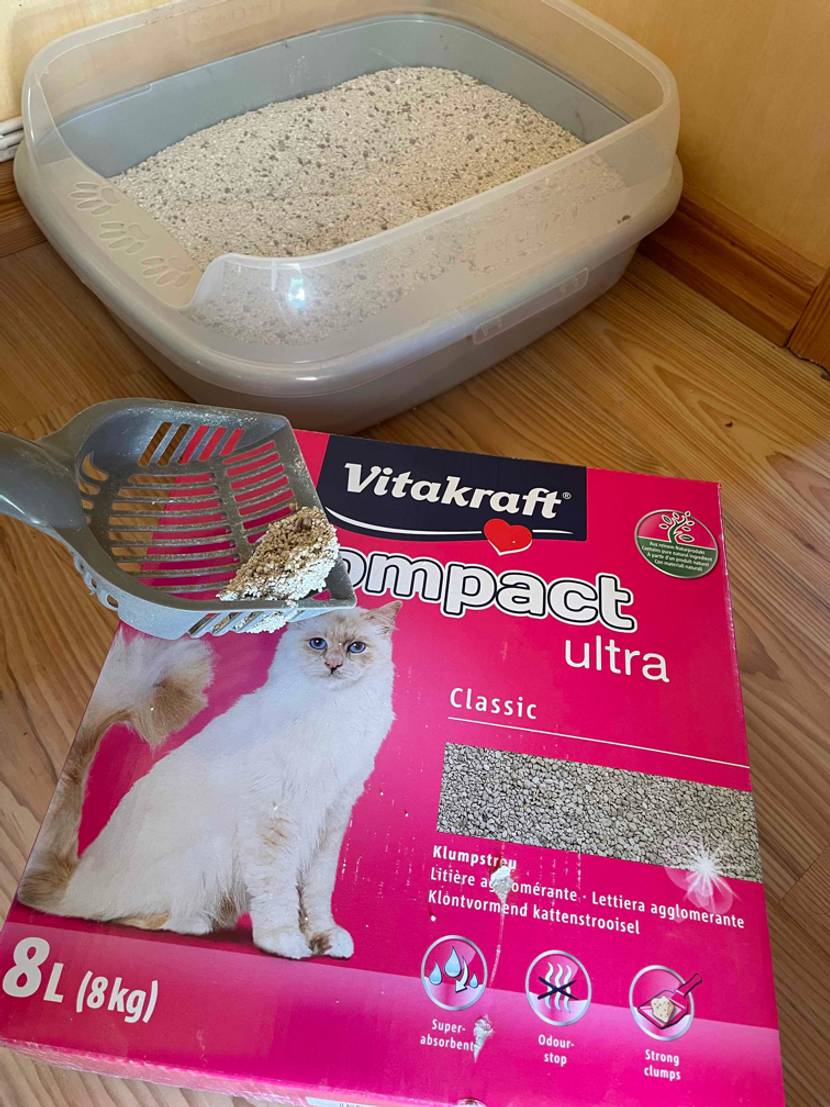Eine liegende Packung Katzenstreu mit einem Katzenklo im Hintergrund