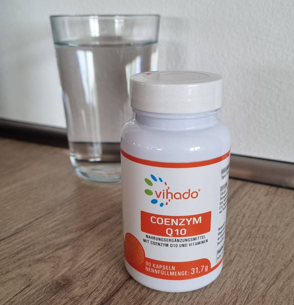 Vihado Coenzym-Q10-Kapseln mit einem Glas Wasser im Hintergrund.
