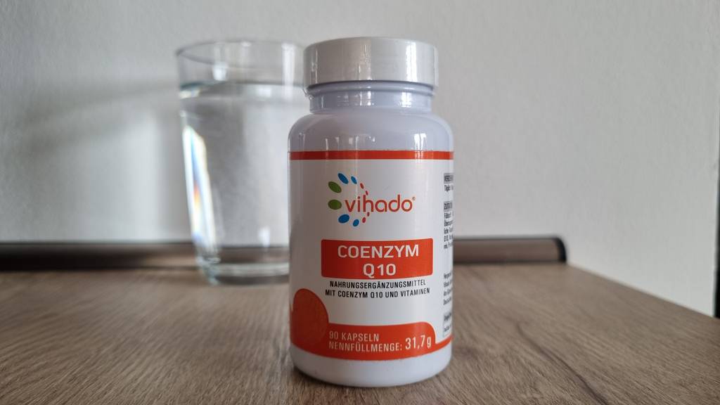 Vihado Coenzym-Q10-Kapseln mit einem Glas Wasser im Hintergrund.