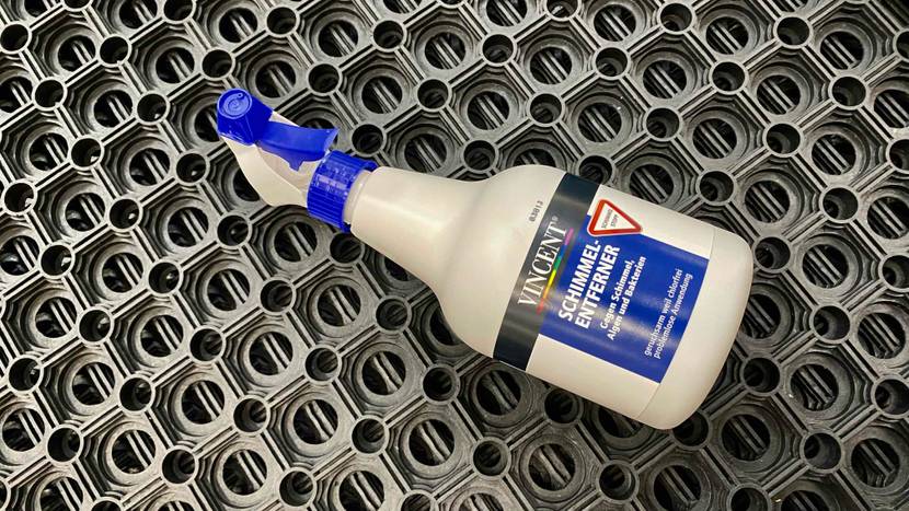 Eine weiße Sprühflasche inklusive getestetem Schimmelentferner von Vincent liegt auf einer grauen, gelöcherten Gummimatte.
