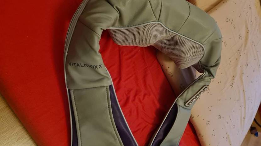 Detailaufnahme eines beigefarbenen Nackenmassagegeräts im Test, das ausgeschaltet auf Bettbezügen liegt.