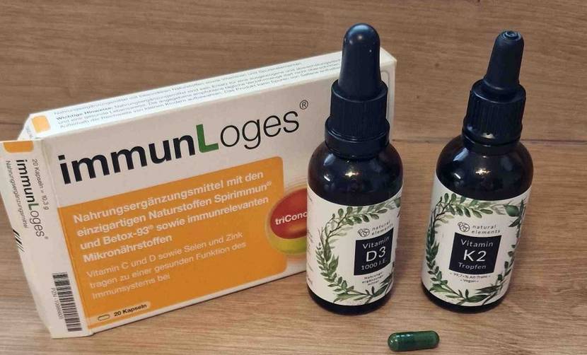 Vitamin-D3-Test: Zwei Flaschen mit Vitamin-Tropfen stehen vor einer Tablettenpackung. Eine einzelne grüne Tablette liegt vor den Flaschen.