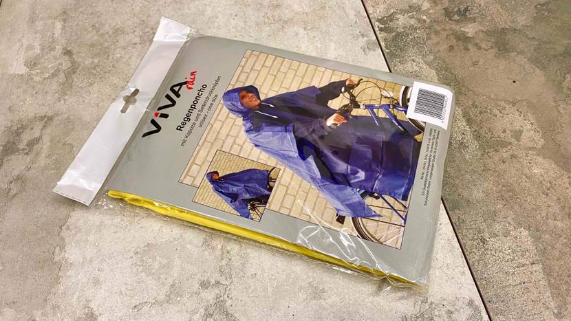 Im Test: Ein originalverpackter gelber Regenponcho liegt auf einer Steinfläche.