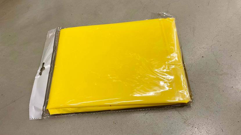 Rückseite eines verpackten gelben Regenponchos im Test auf einer grauen Fläche liegend.