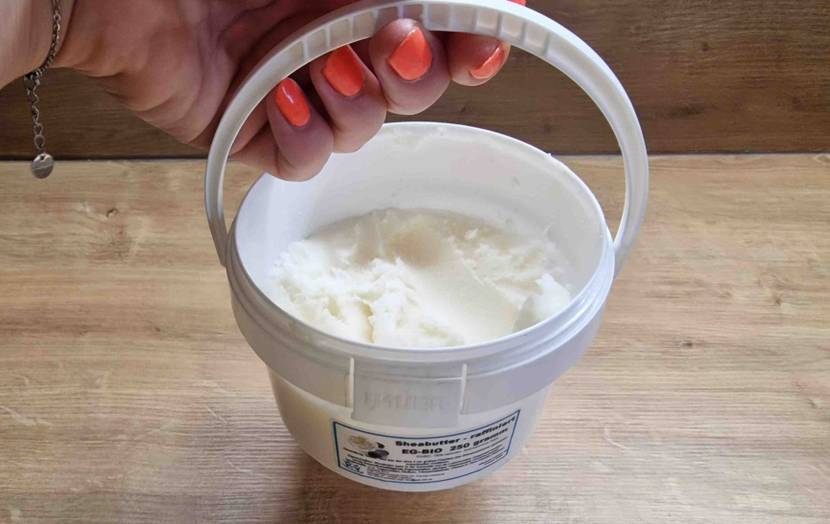 Sheabutter-Test: Hand stellt weißen Behälter mit Sheabutter auf einen Holztisch.