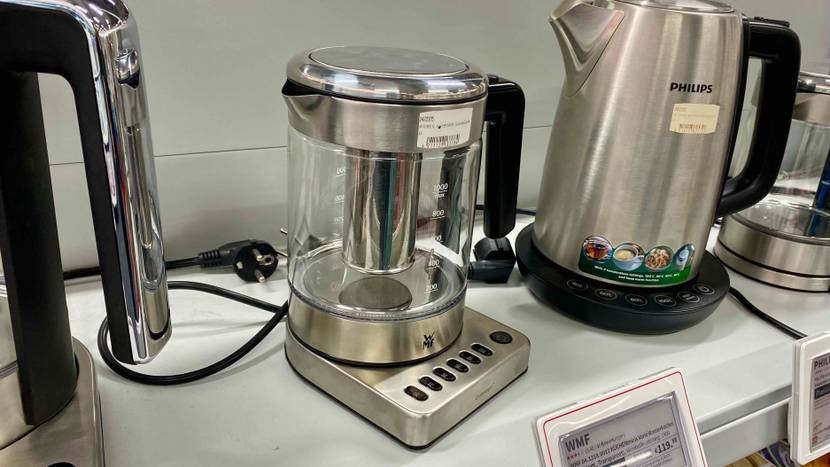 Im Test: Ein Wasserkocher mit Temperatureinstellung von schräg seitlich vor anderen Produkten auf einem Verkaufsregal mit Preisangabe.