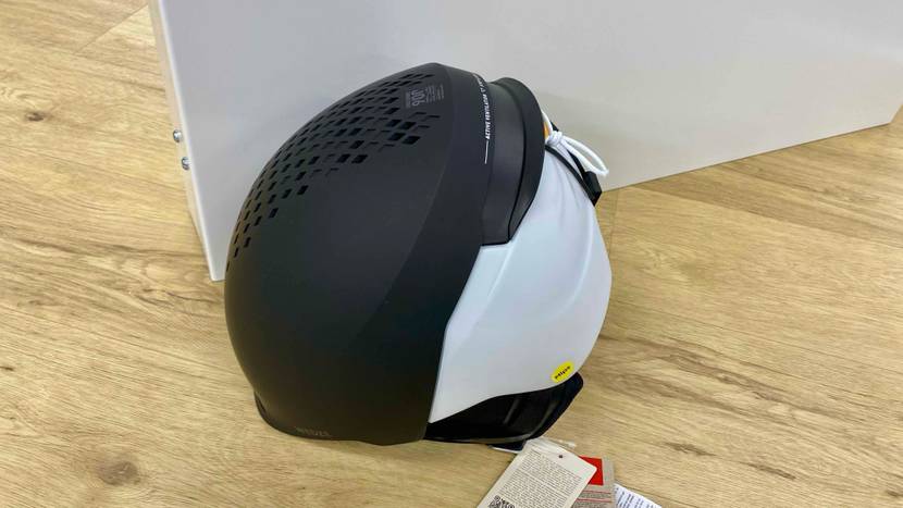 Ein getesteter Skihelm in schwarz-weiß von der Seite vor einer hellen Fläche auf einem Holzboden.