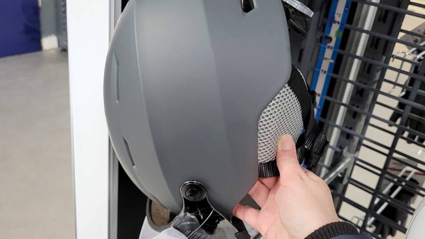 Hand fühlt das Stoffmaterial des Ohrschutzes von einem grauen Skihelm mit Visier im Test, der im Verkauf ausgestellt ist.