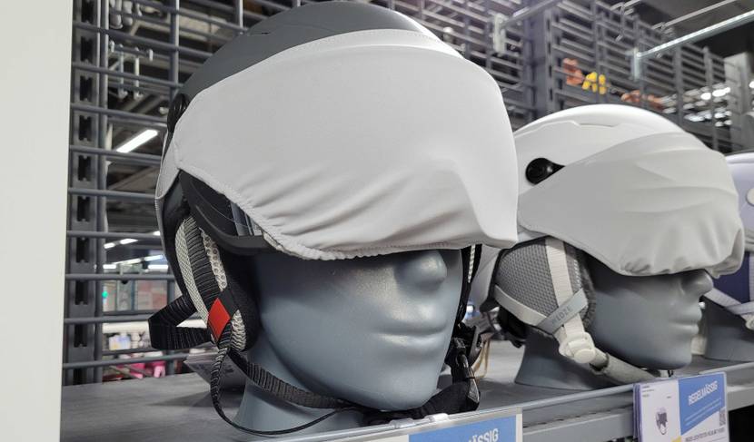Auf einem Verkaufsregal befinden sich zwei Puppenköpfe mit grauen Skihelmen mit Visier im Test, deren Visier mit einer hellgrauen Schutzhaube abgedeckt ist.
