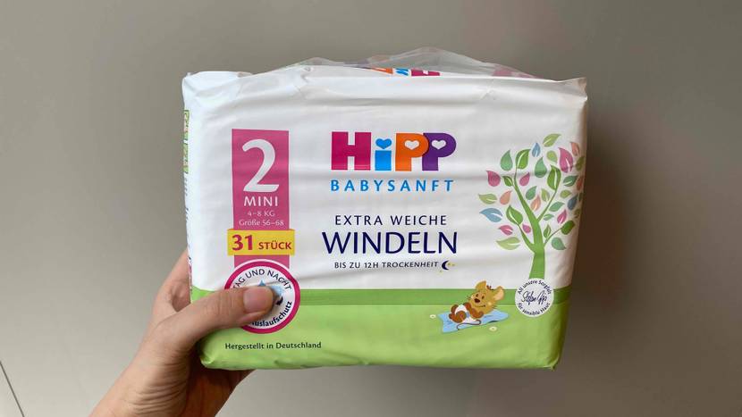 Eine Hand hält eine Packung der getesteten Windeln vor eine helle Wand.