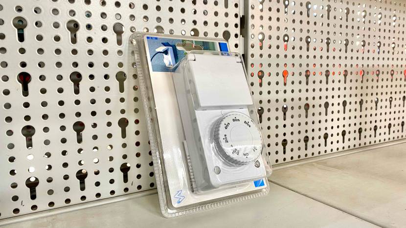 Zeitschaltuhr getestet: Eine verpackte Uhr leicht schräg vor einem Lochblech.