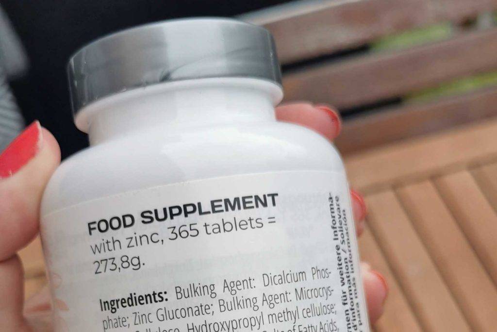 Hand hält eine Dose Zinktabletten, die die Inhaltsstoffe anzeigt.