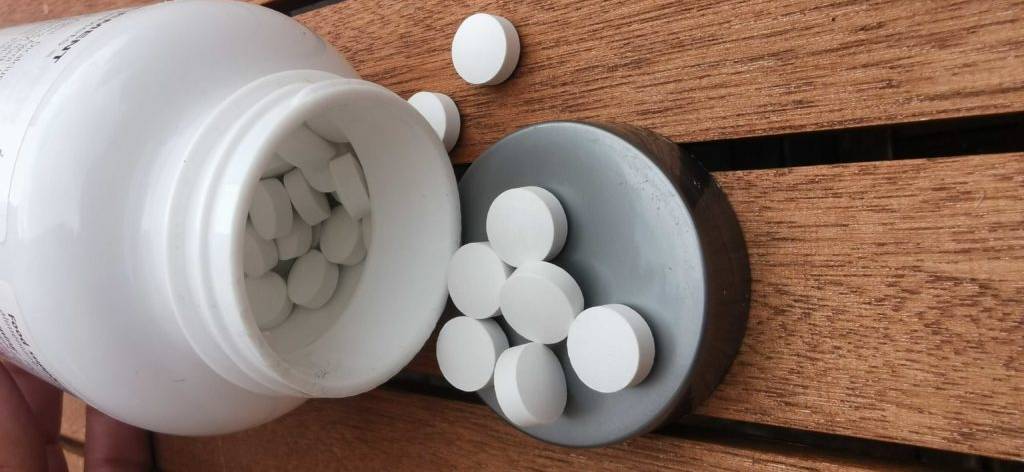 Eine Dose Tabletten liegt offen auf einem Holztisch, einige Tabletten auf dem Deckel.